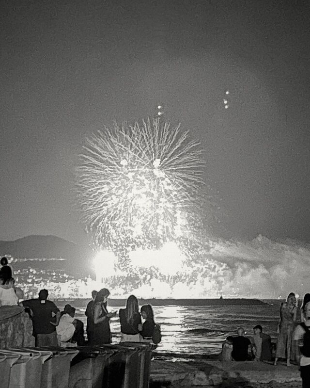 Fireworks over the sea, watched by people standing on the beach in Sitges.